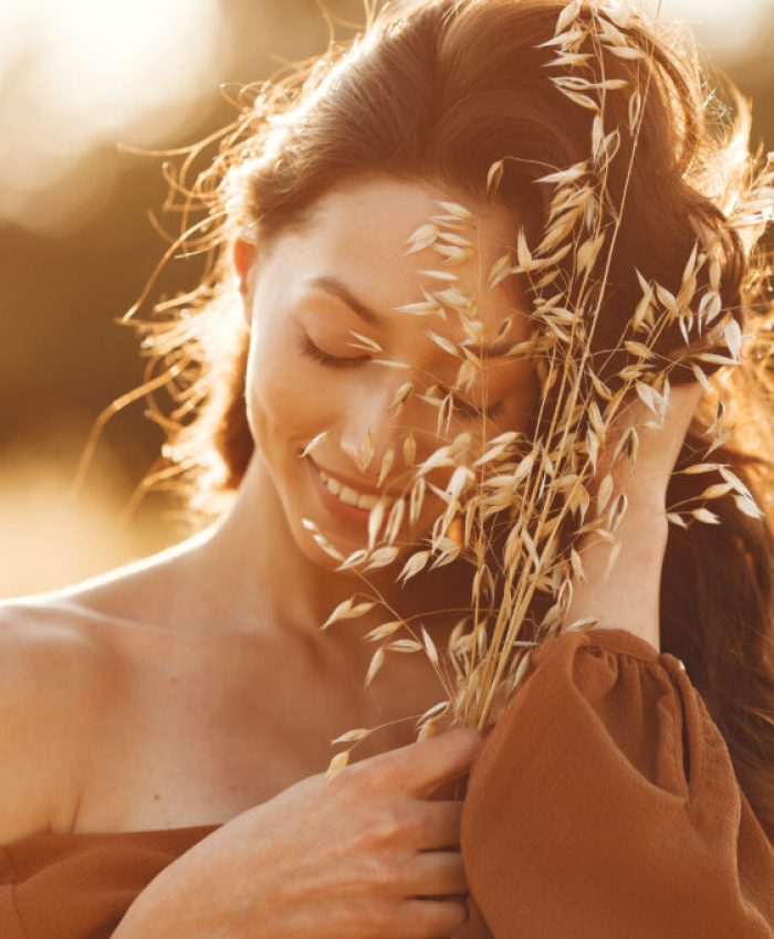 Woman in a summer field. Brunette in a brown sweater. Girl on a sunset background.
